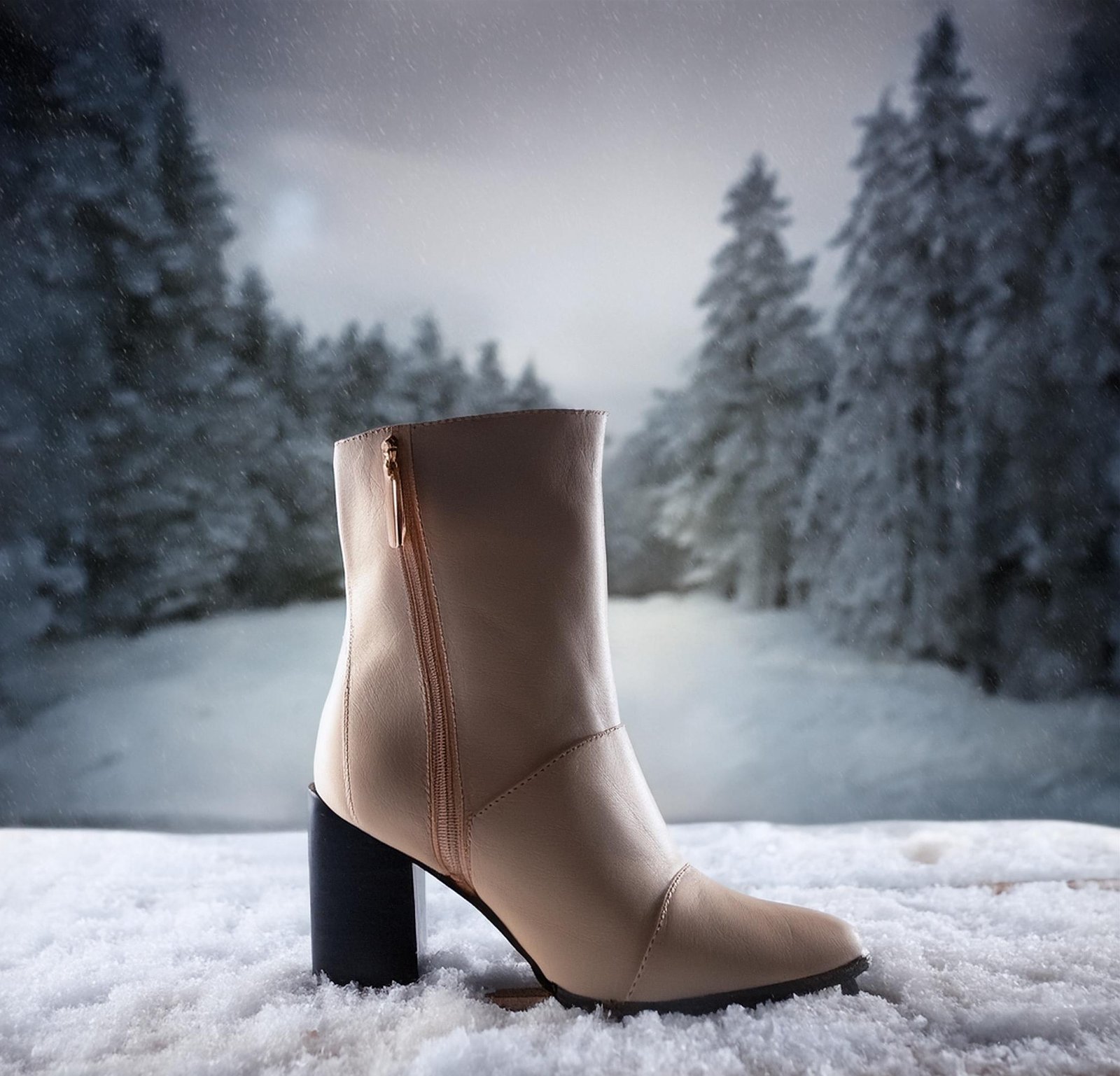 A stylish beige heeled boot with a zipper stands elegantly on the snow, set against a wintry forest backdrop, embodying both comfort and sophistication.